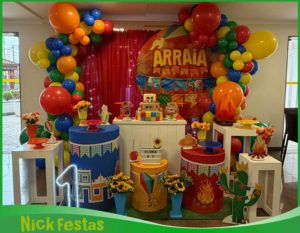 Decoração infantil Festa Junina montada em salão de festas com painel temático, bandeirinhas coloridas, balões, fogueira cenográfica, cactos decorativos, mesa personalizada e elementos caipiras para aniversário infantil na Freguesia do Ó, São Paulo.