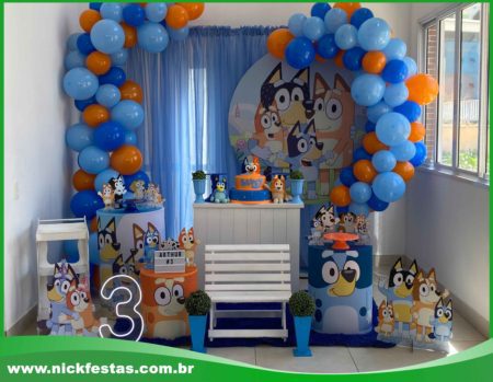 Decoração de festa infantil com tema Bluey, incluindo painel colorido, mesas decoradas e personagens da série.