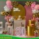 Decoração 80 anos rosa e dourado com arco de balões, painel elegante, mesa decorada e detalhes sofisticados para aniversário na Freguesia do Ó SP
