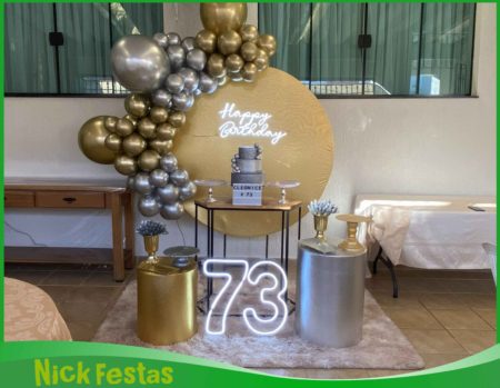 Decoração dourado e prata para festa de 70 anos, com painel decorativo, arco de balões, mesa principal e elementos sofisticados para comemoração de aniversário.
