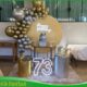 Decoração dourado e prata para festa de 70 anos, com painel decorativo, arco de balões, mesa principal e elementos sofisticados para comemoração de aniversário.