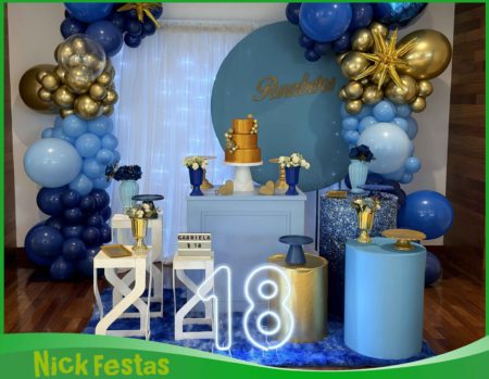 Decoração azul e dourado para festa de 18 anos, com painel decorativo, arco de balões, mesa principal e elementos em tons de azul e dourado.