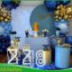 Decoração azul e dourado para festa de 18 anos, com painel decorativo, arco de balões, mesa principal e elementos em tons de azul e dourado.