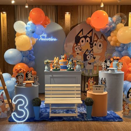 Decoração infantil tema Bluey para locação, com painel personalizado, personagens, mesa decorativa e arco orgânico de balões em azul, laranja, branco e amarelo.