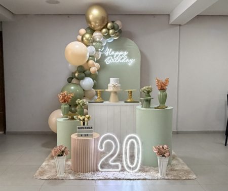 Decoração para festa em tons de verde eucalipto e bege, com painel decorativo, arco orgânico de balões, mesa principal, cilindros e detalhes elegantes para comemoração.